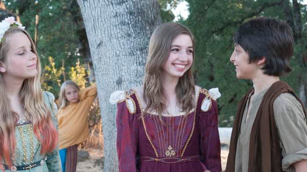 Two teenage actors in Renaissance costume, laughing, among the trees.
