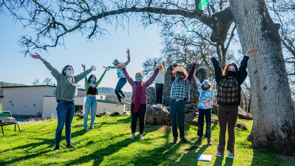 The young company leaping with arms raised beneath the oak, several of them wearing masks.